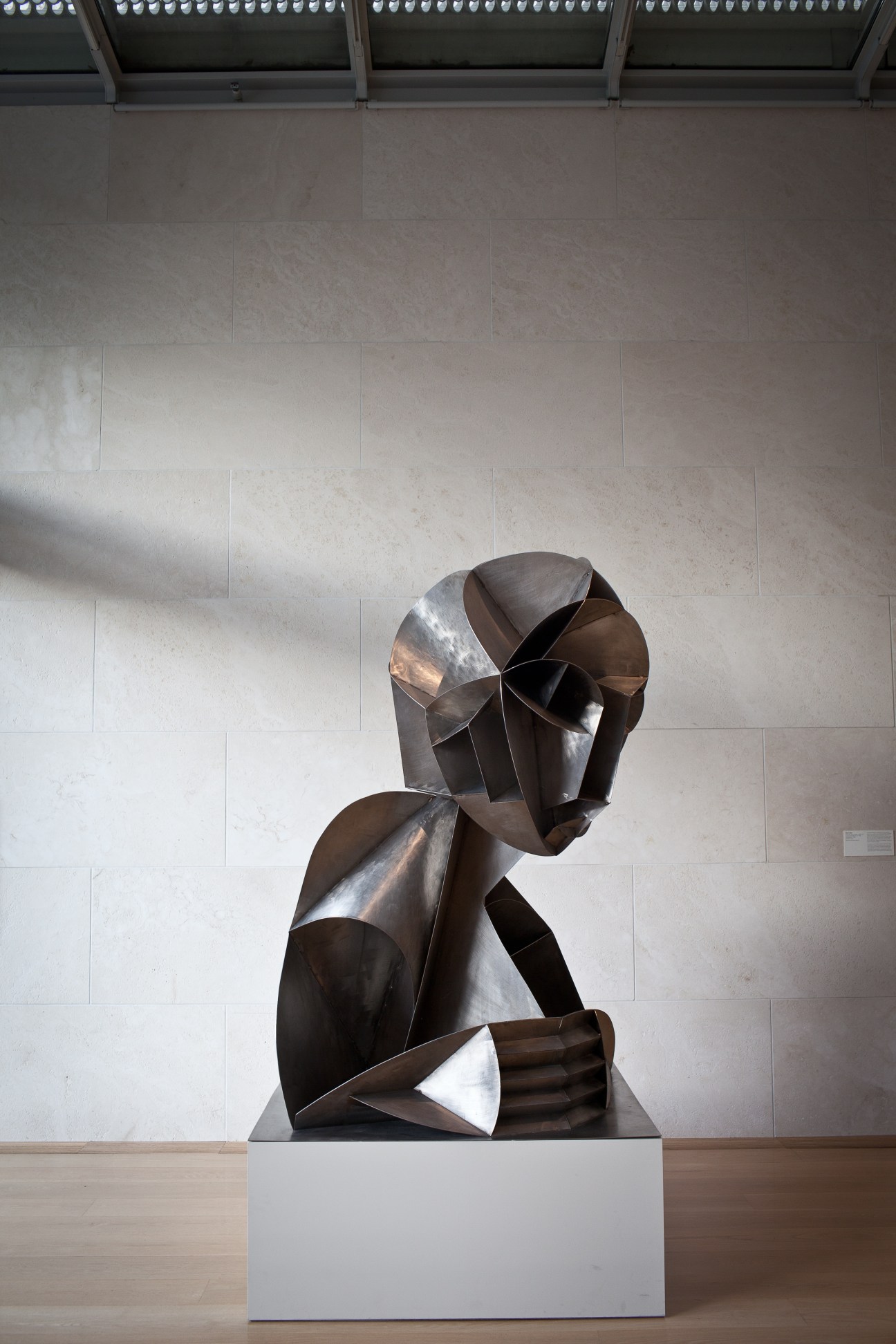 Abstract bronze sculptural bust with geometric angular forms displayed in a modern gallery space with white walls.