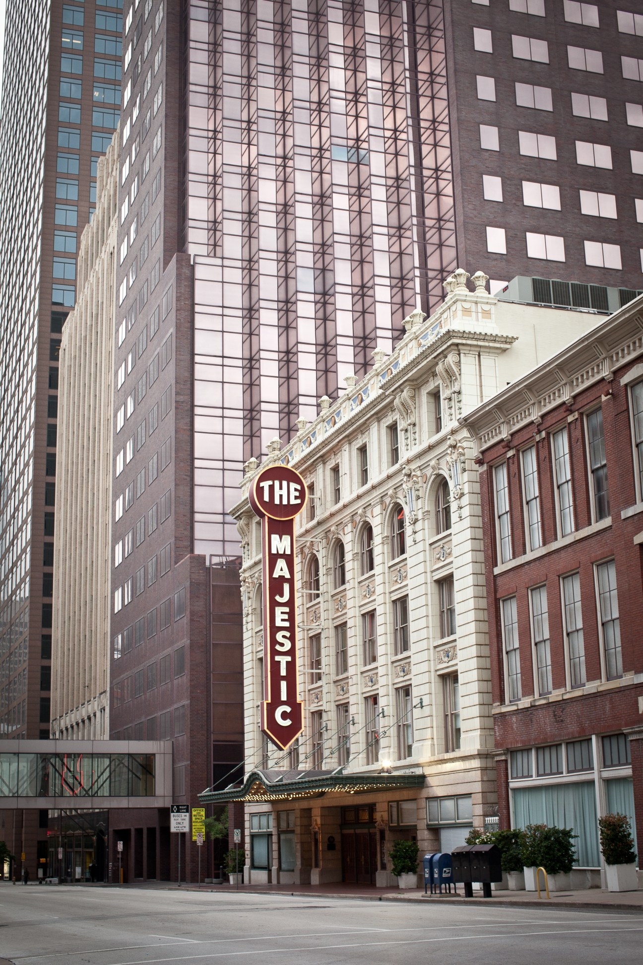 The Majestic Theatre's ornate cream and red facade with vertical signage, flanked by modern downtown Dallas skyscrapers.