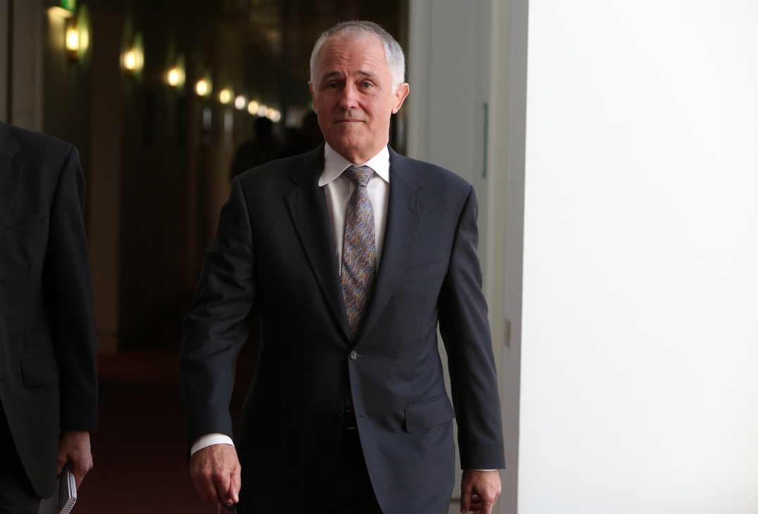 Man in dark business suit walking through a hallway with formal lighting.