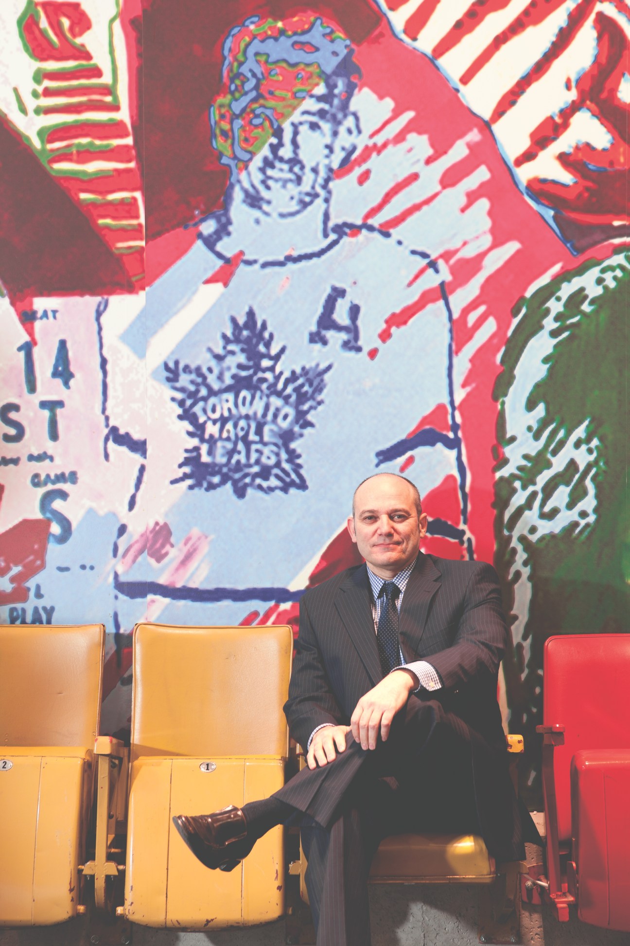 Mario Fatica sits on yellow arena seating with Toronto Maple Leafs artwork behind him.