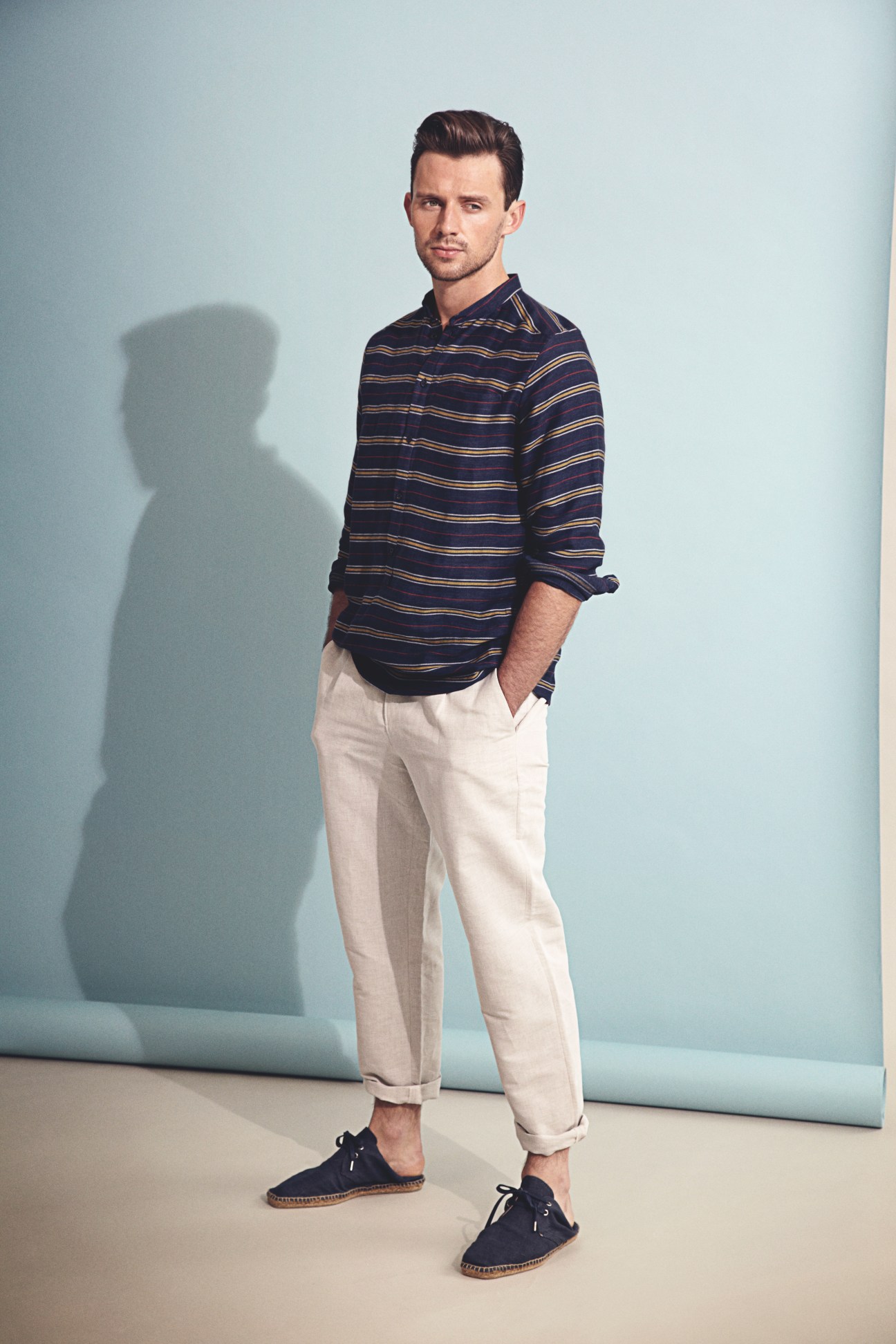 Man wearing navy striped shirt and cream chinos in studio portrait