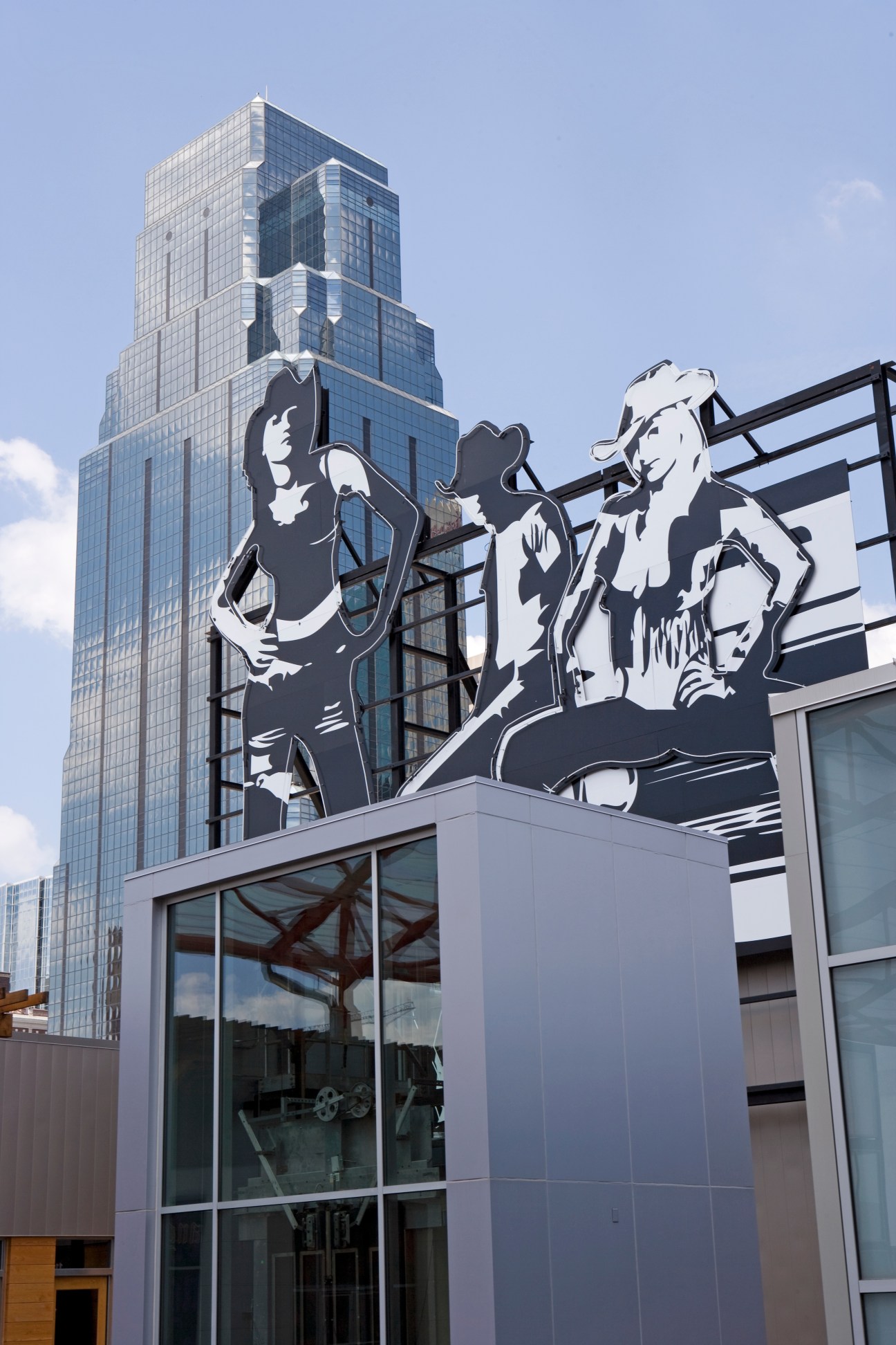 Large black and white billboard depicting three figures in Kansas City's Power & Light District with modern skyscraper behind.