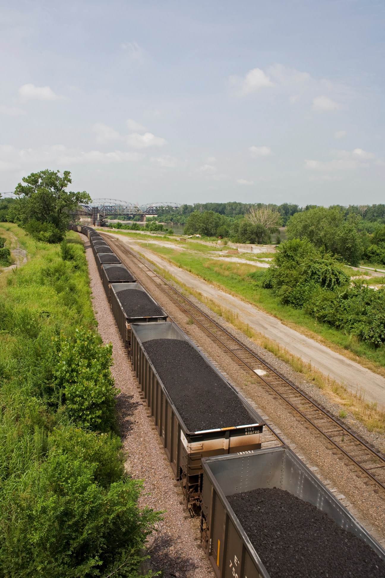 Freight train loaded with coal cars on railroad tracks in rural Kansas City landscape.