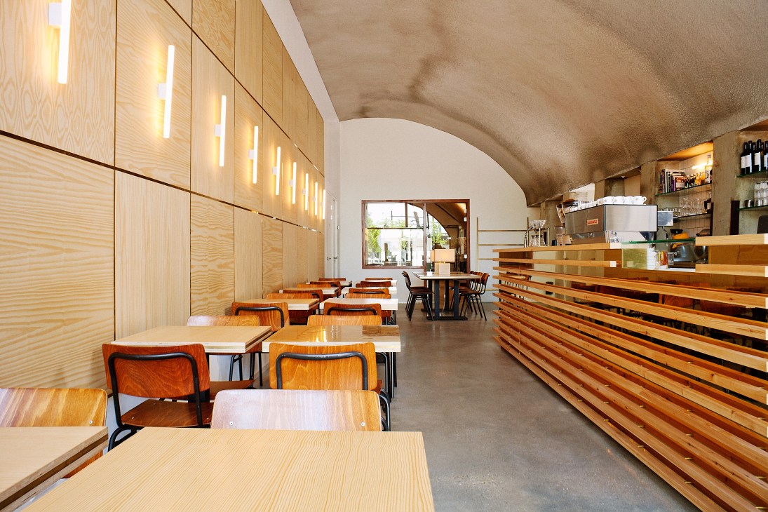Interior of Lokaal Coffee in Rotterdam with wooden tables, chairs, and pine-wood cabinetry under arched ceiling.