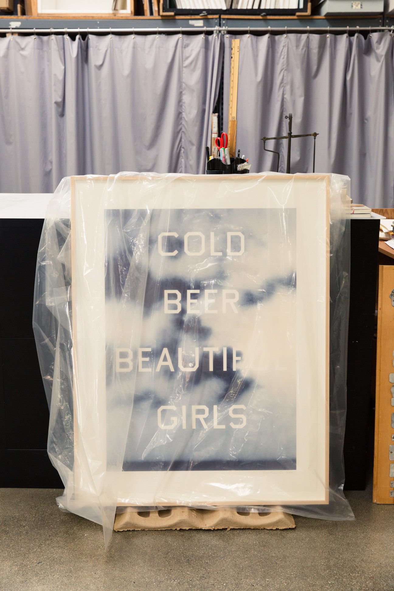 Wrapped painting with "COLD BEER BEAUTIFUL GIRLS" text displayed in Ruscha's studio library.