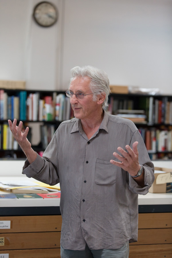 Artist Ed Ruscha gestures while speaking in his Culver City studio, with bookshelves and a wall clock visible behind him.