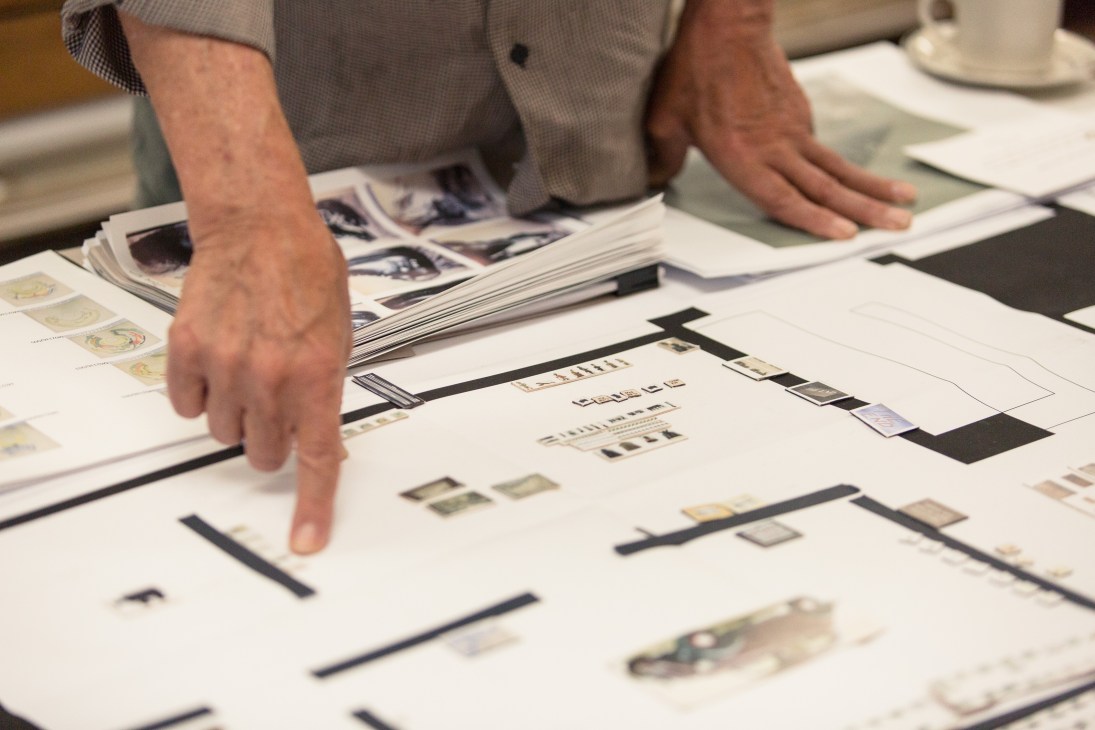 Person pointing at layout sketches and color swatches on white table during art planning session