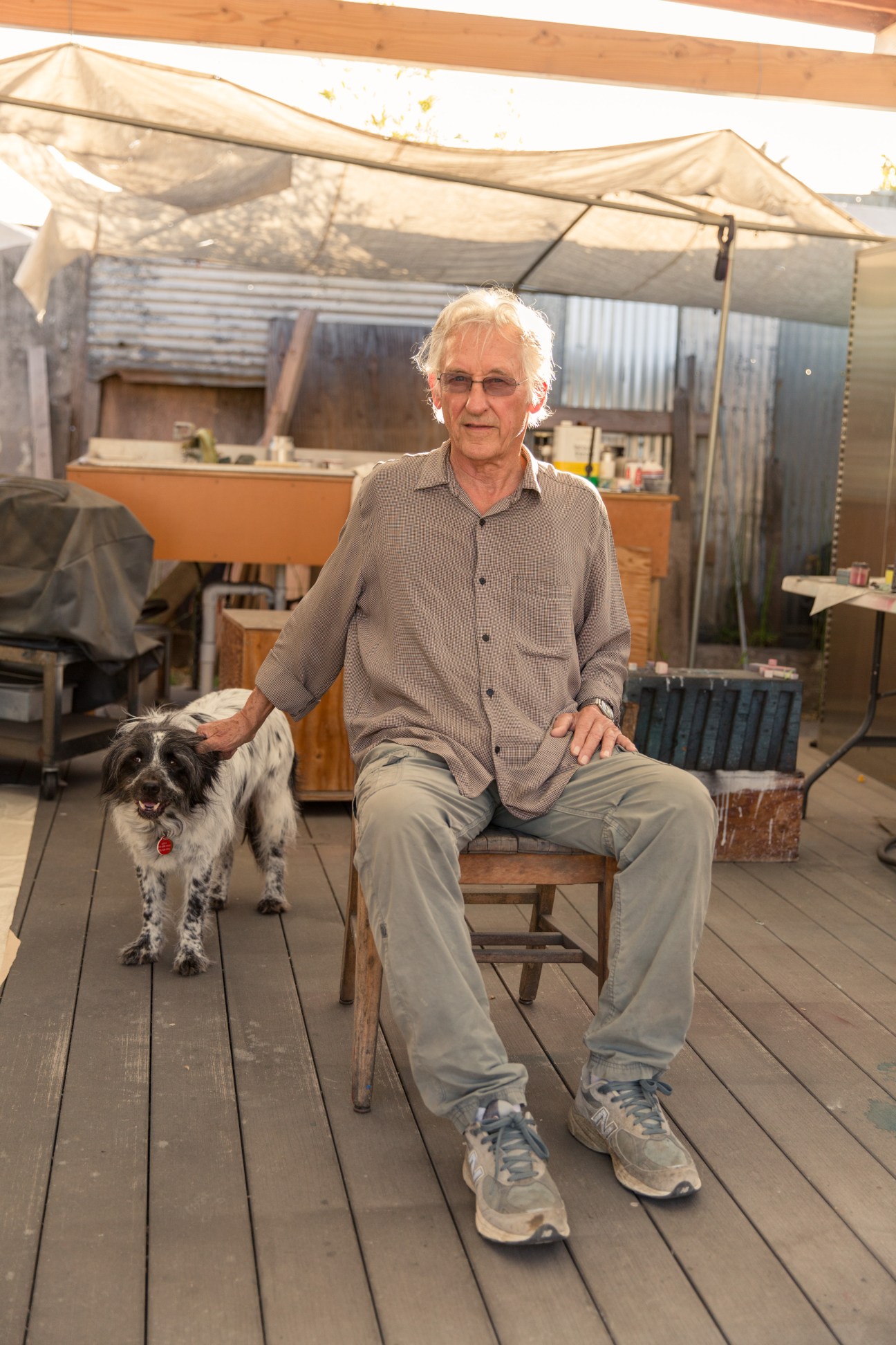 Artist Ed Ruscha sits on a wooden chair in his Culver City studio courtyard with his dog Lola beside him.