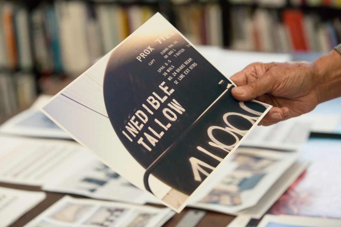 Hand holding a book with text reading "INEDIBLE TALLOW" against a library backdrop.