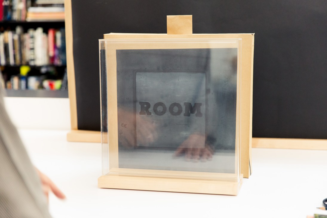Wooden framing glass display of Ed Ruscha artwork with "ROOM" text visible inside.