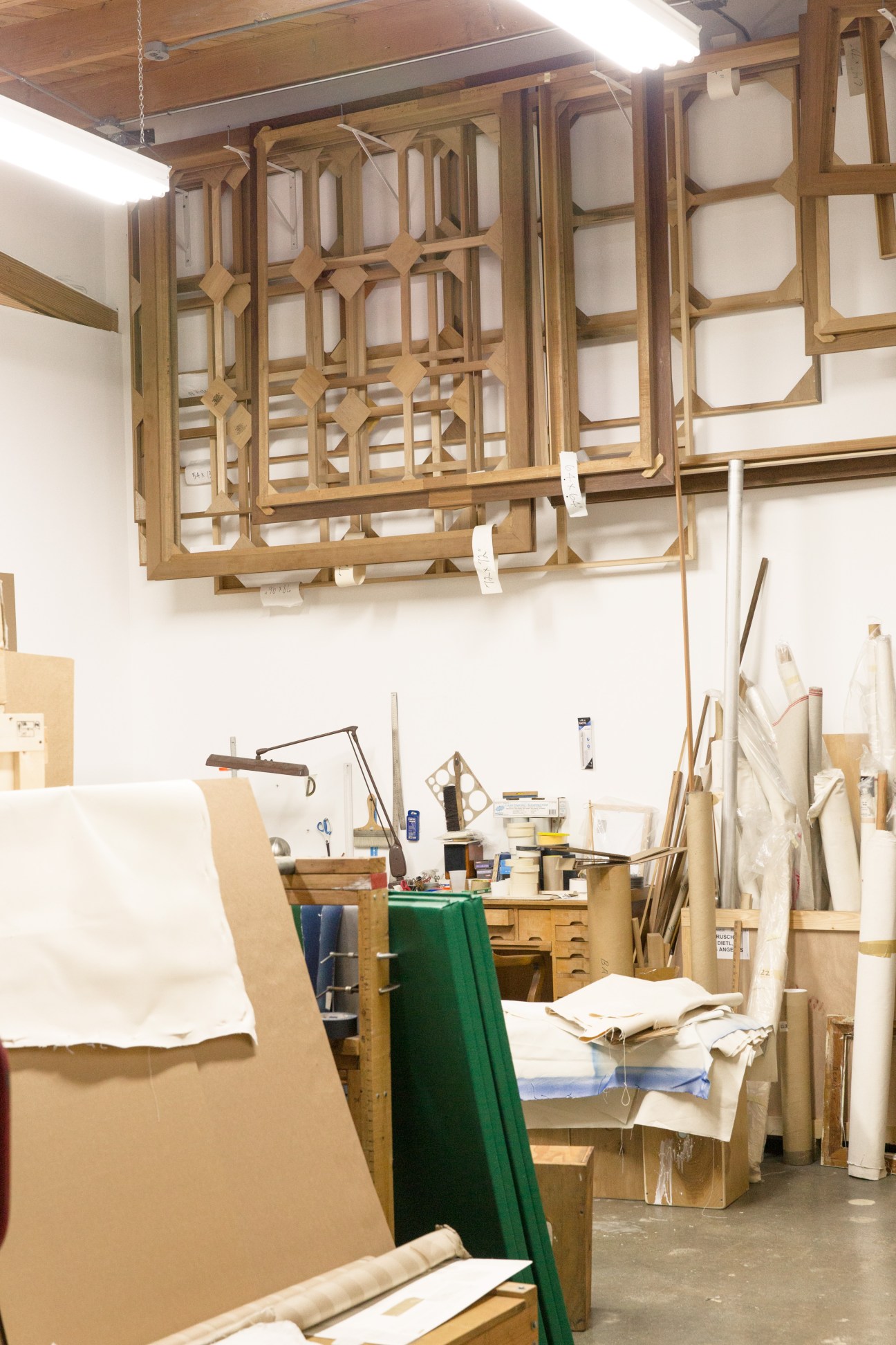 Wooden framed glass panels hung from ceiling above canvas and artwork materials in a studio workspace.