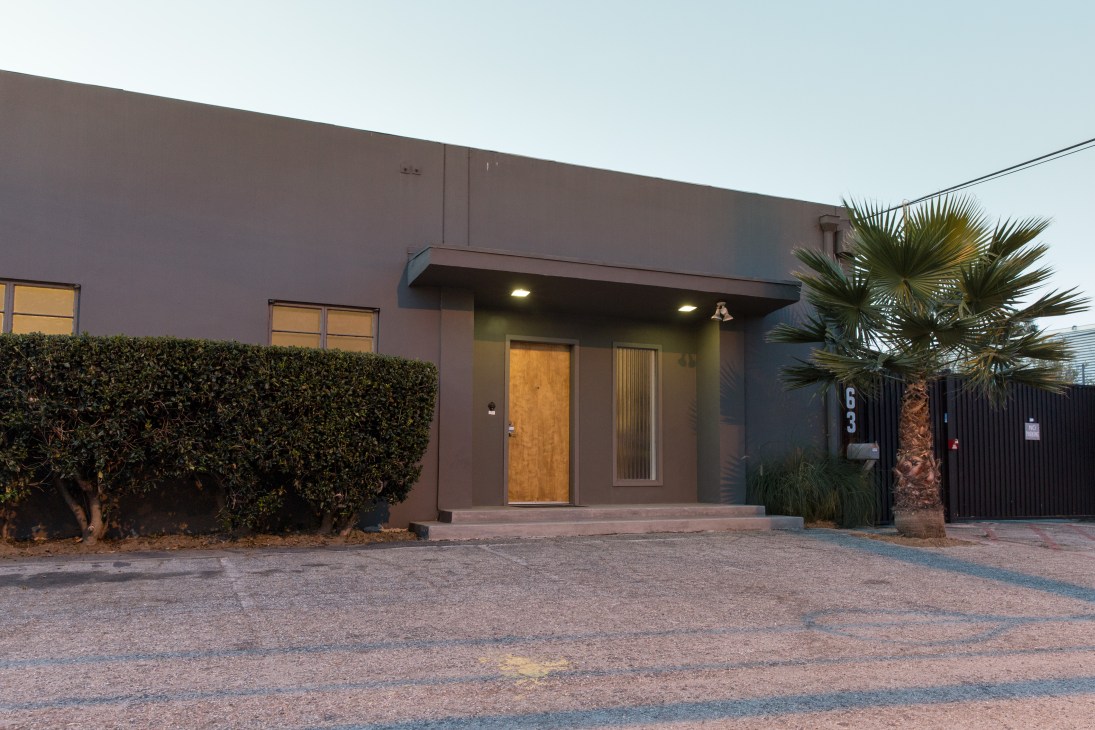 Exterior of Ed Ruscha's Culver City studio, a modernist brown building with palm tree and hedge landscaping.