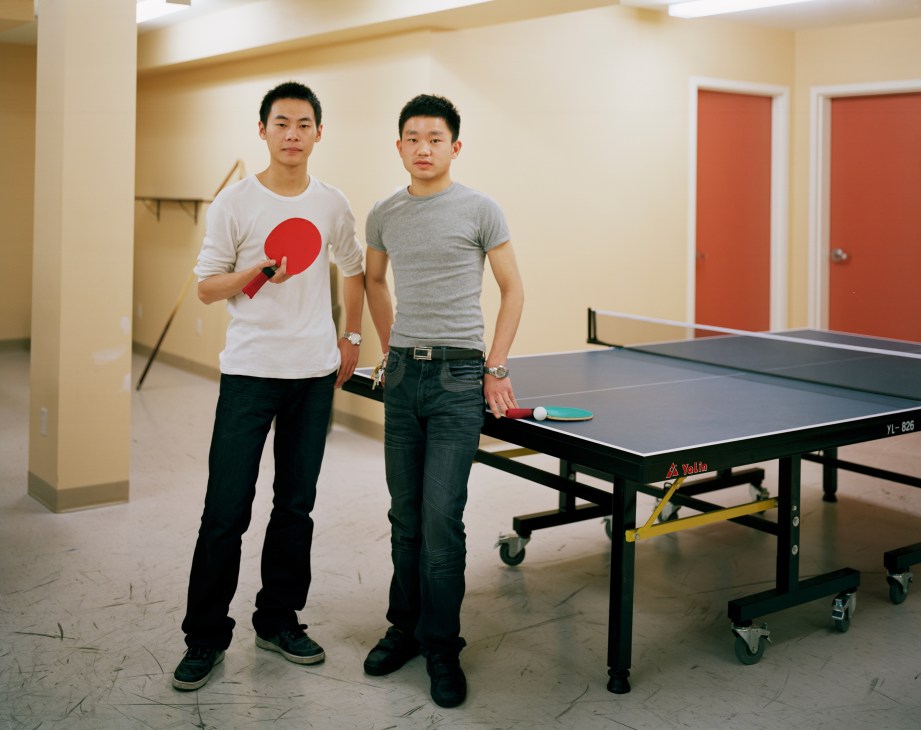 Two young Chinese male students standing beside a ping pong table, one holding a paddle.