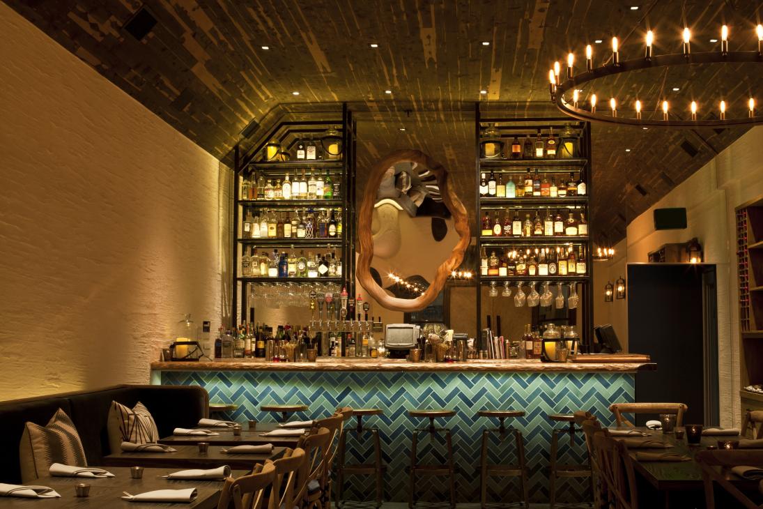 Wolf restaurant interior with illuminated bar shelves, herringbone tile backsplash, and decorative sculptural artwork.
