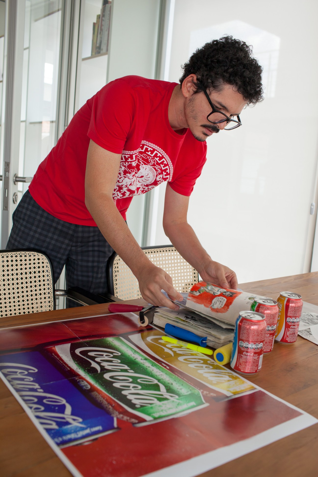 Man in red shirt examining Coca-Cola cans in Brazil flag colors on table.