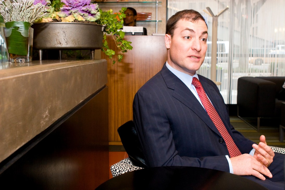Sean McFate, former project manager at DynCorp, sits in an office wearing a dark suit and red tie.