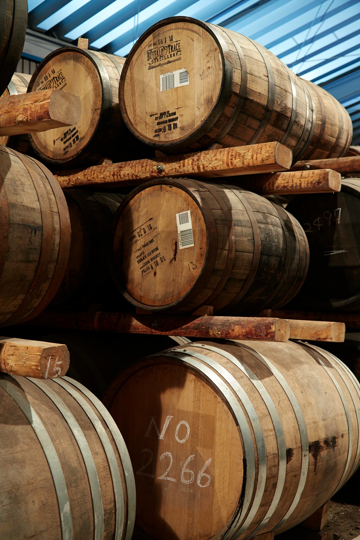 Wooden whisky barrels stacked in rows at Chichibu Distillery warehouse with blue skylight overhead.