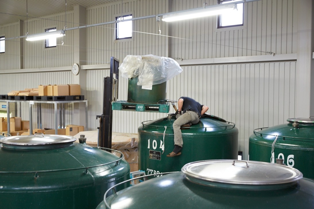 Worker leaning over a large green fermentation tank labeled 104 at Chichibu Distillery.