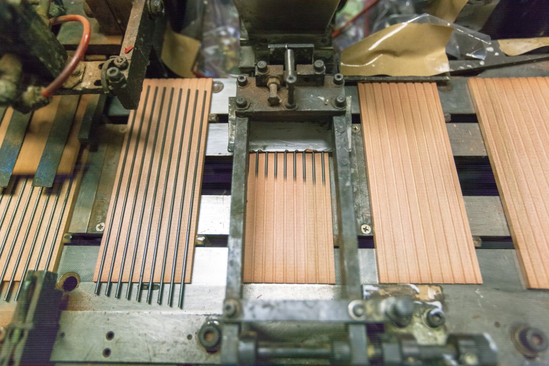 Industrial machinery with wooden pencil casts arranged in metal frames during manufacturing.