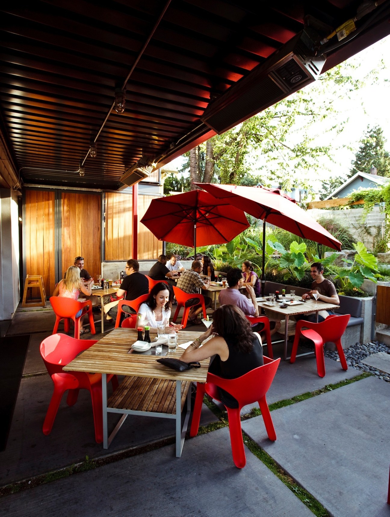Outdoor patio dining area with red chairs, wooden tables, and red umbrellas at Yakuza restaurant in Portland.