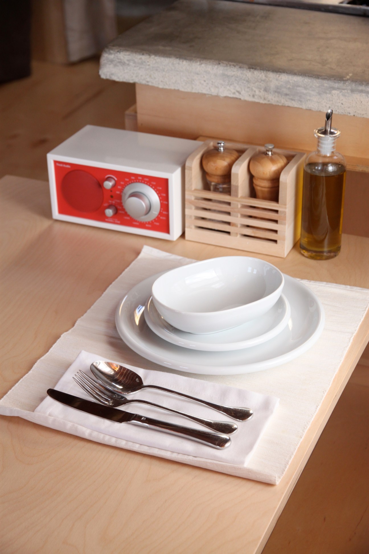 Minimalist table setting with white dishes, cutlery, red radio, wooden salt and pepper shakers, and oil bottle at Yakuza Garden Cottage.