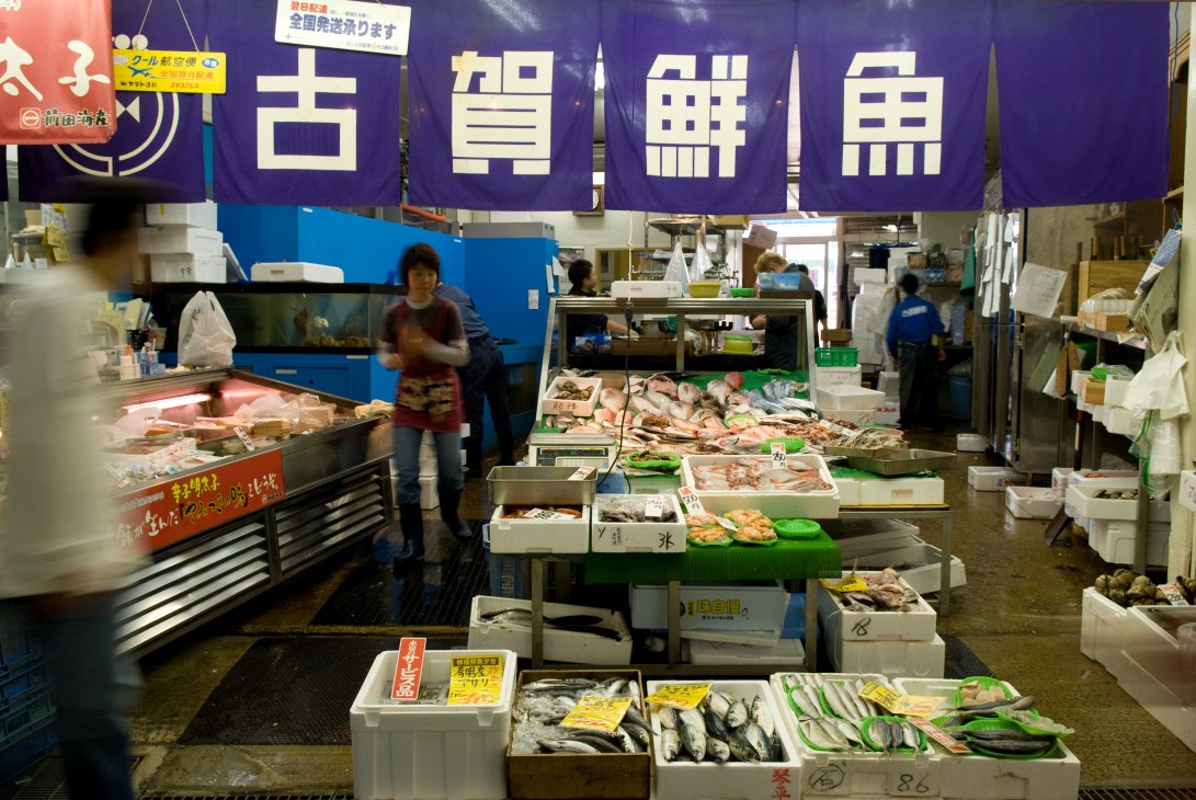 Busy fish market stall at Yanagibashi market with vendors and fresh seafood displays under purple signage.