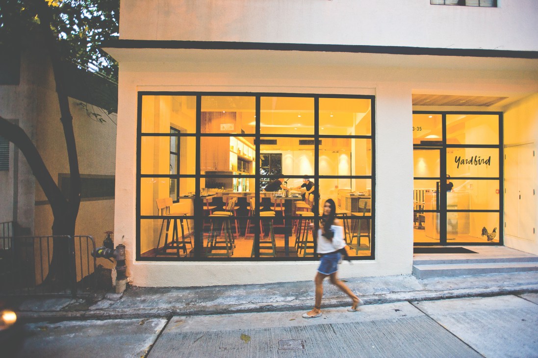 Exterior of Yardbird yakitori restaurant in Hong Kong's Sheung Wan with illuminated storefront and diners visible inside.