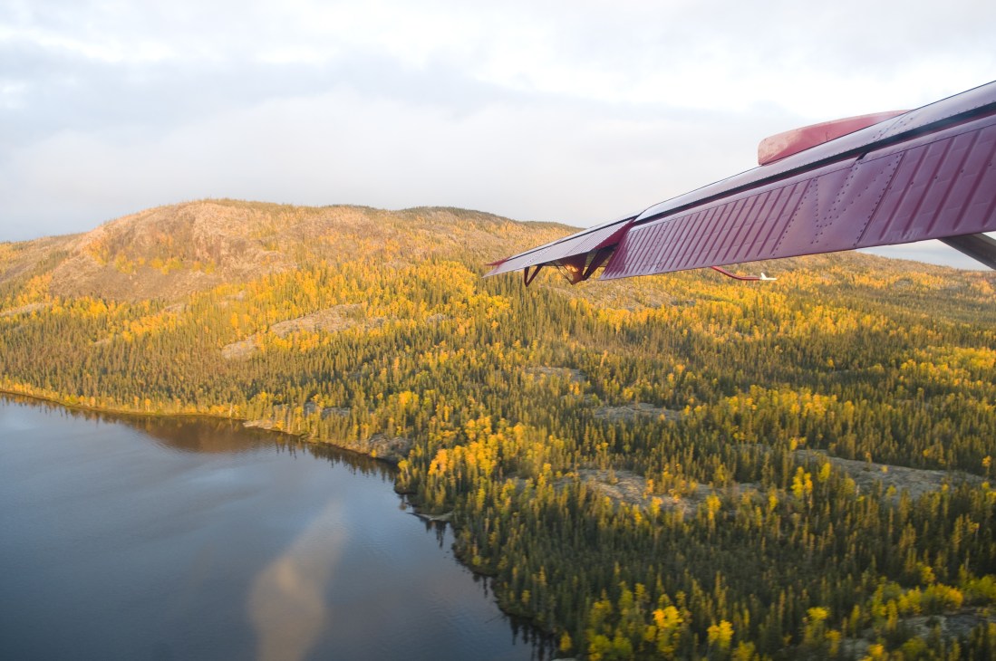 Aerial view of a seaplane flying over forested landscape with lakes and autumn foliage in Northwest Territories.