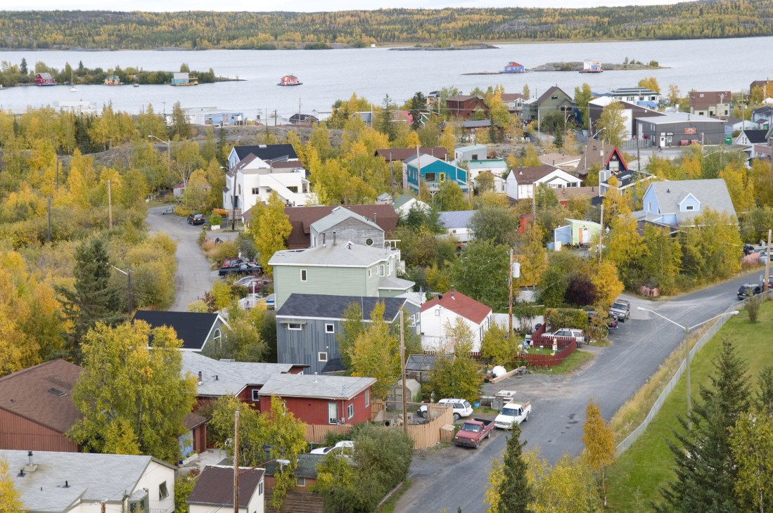 Aerial view of Yellowknife old town with colorful houses, boats on Great Slave Lake, and autumn foliage.
