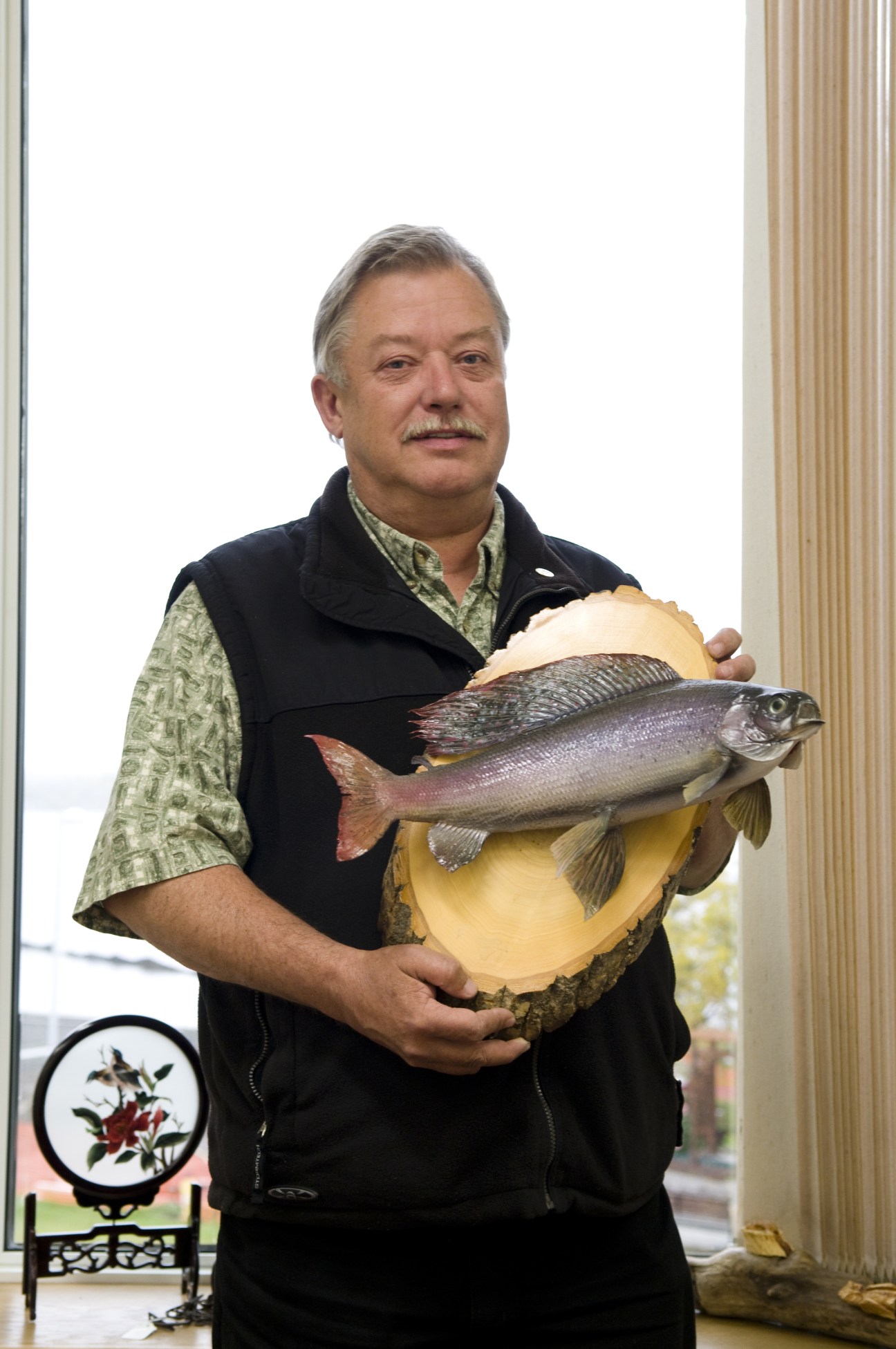 Yellowknife mayor Gordon Van Tighem holding a large Arctic char fish mounted on wood.