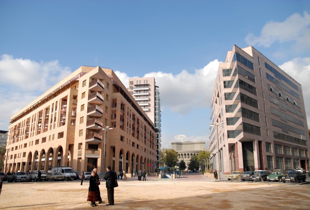 Modern apartment buildings surrounding a public square in Yerevan, Armenia with people walking in the plaza.