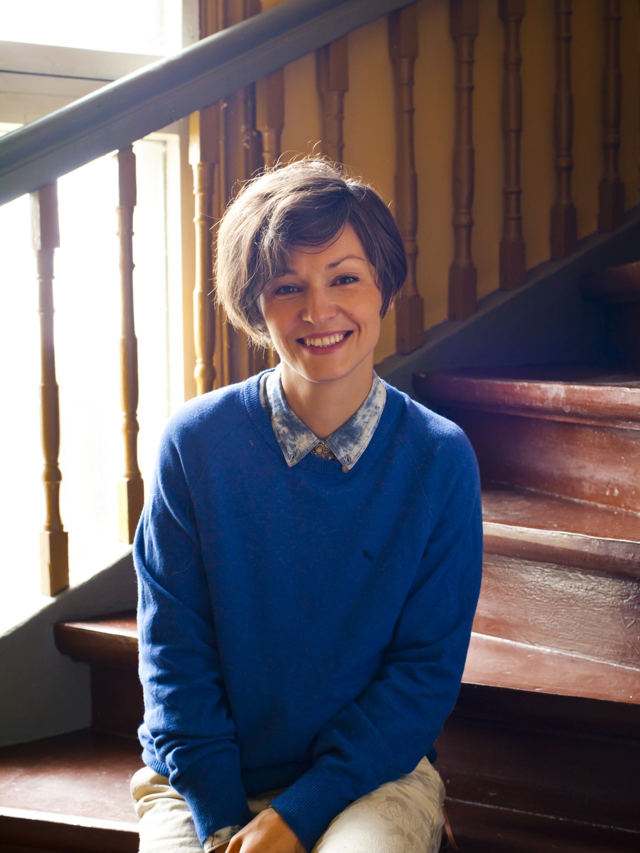 Portrait of Yoko Alender, F Hoone co-founder, smiling on wooden stairs in a Kalamaja home.