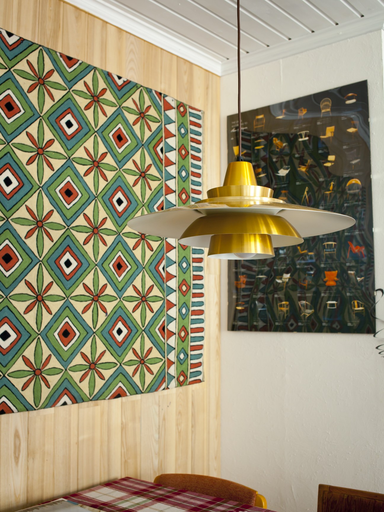 Modern kitchen interior with geometric patterned wallpaper, brass pendant light, and artwork on white walls.