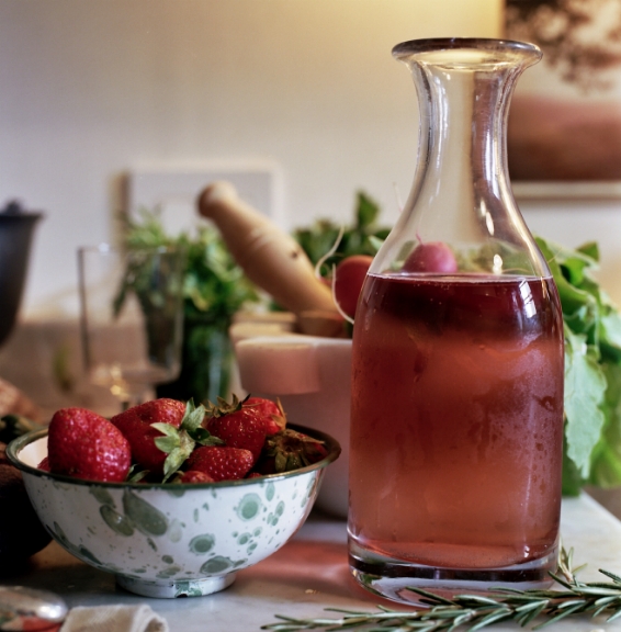 A carafe of rosé wine next to a bowl of fresh spring strawberries with herbs and kitchen items in the background.
