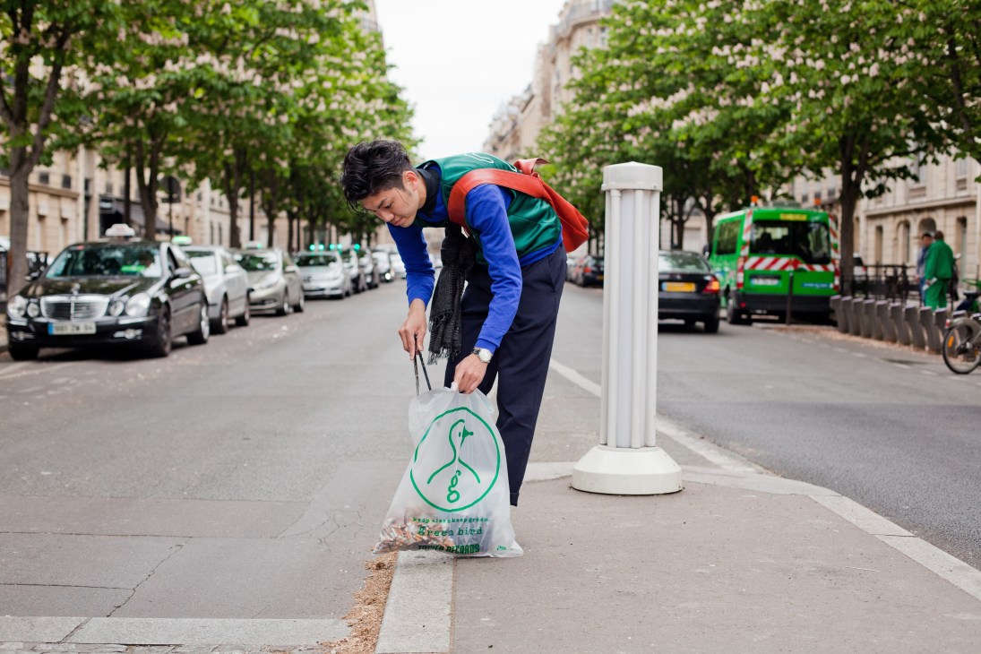 Green Bird volunteer Kenta Usui collecting litter on a Paris street with tongs and branded bag.