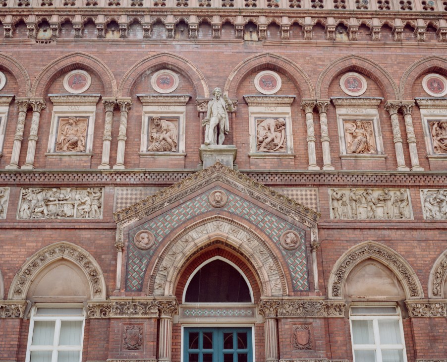 Ornate red brick Victorian building facade with ceramic relief panels and decorative arched doorway