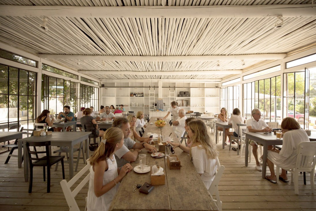 Diners gather in a light-filled restaurant with corrugated metal ceiling and large windows at La Linda bakery.
