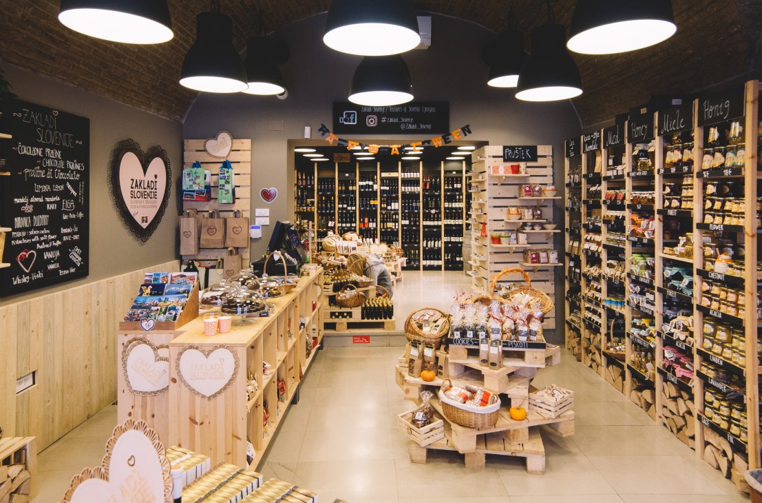 Interior of Zakladi Slovenije delicatessen with wooden shelving displaying Slovenian products, oils, chocolates and wines.
