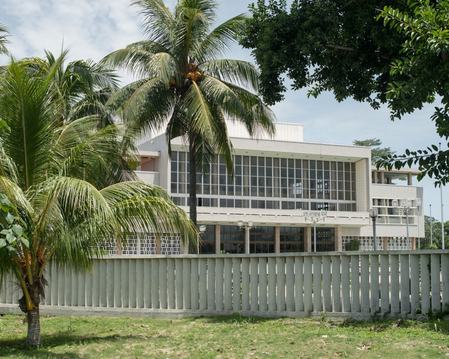 São Tomé's parliament building with palm trees and tropical vegetation in the foreground.