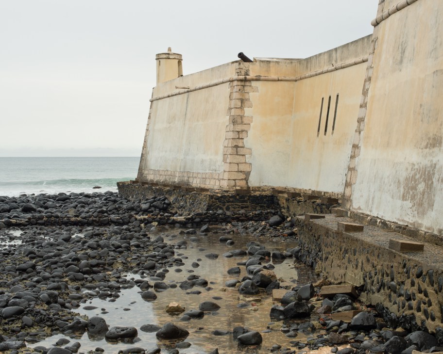 Weathered Portuguese fort seafront with cannons protruding from stone walls overlooking rocky beach.