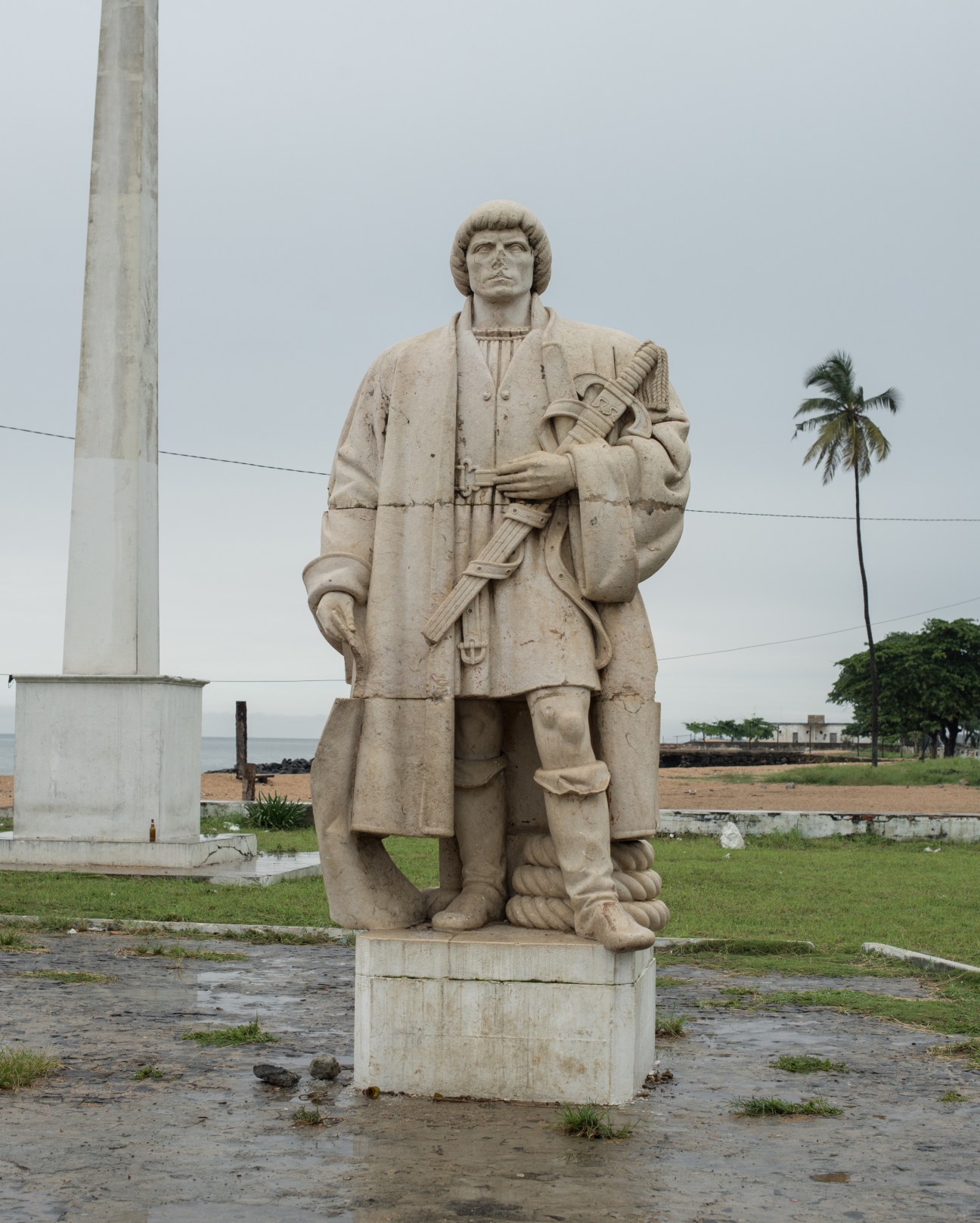 Stone statue of a Portuguese explorer holding a sword, standing on pedestal in São Tomé