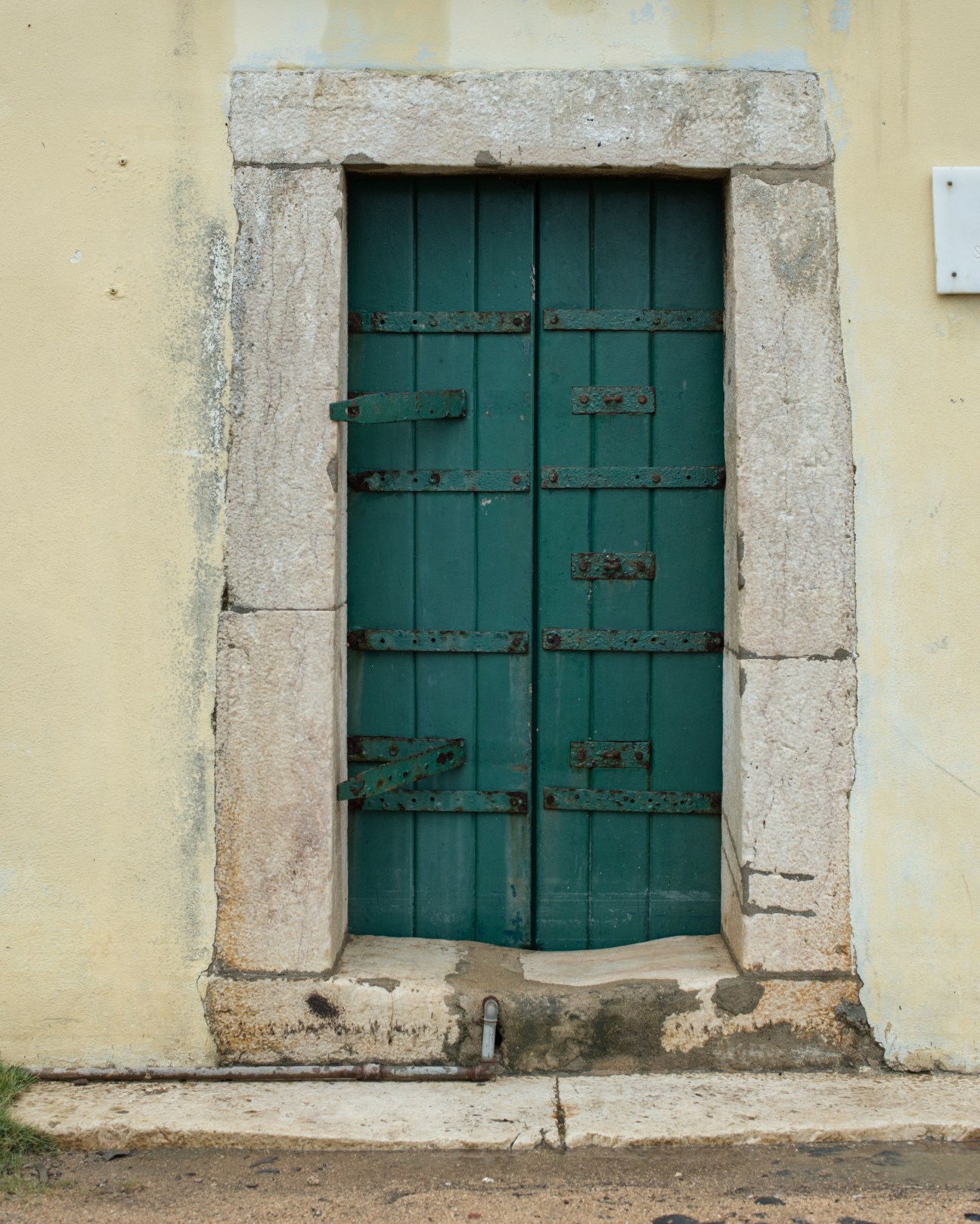 Green wooden door with rusted metal hinges on a cream-colored stone fortification wall.