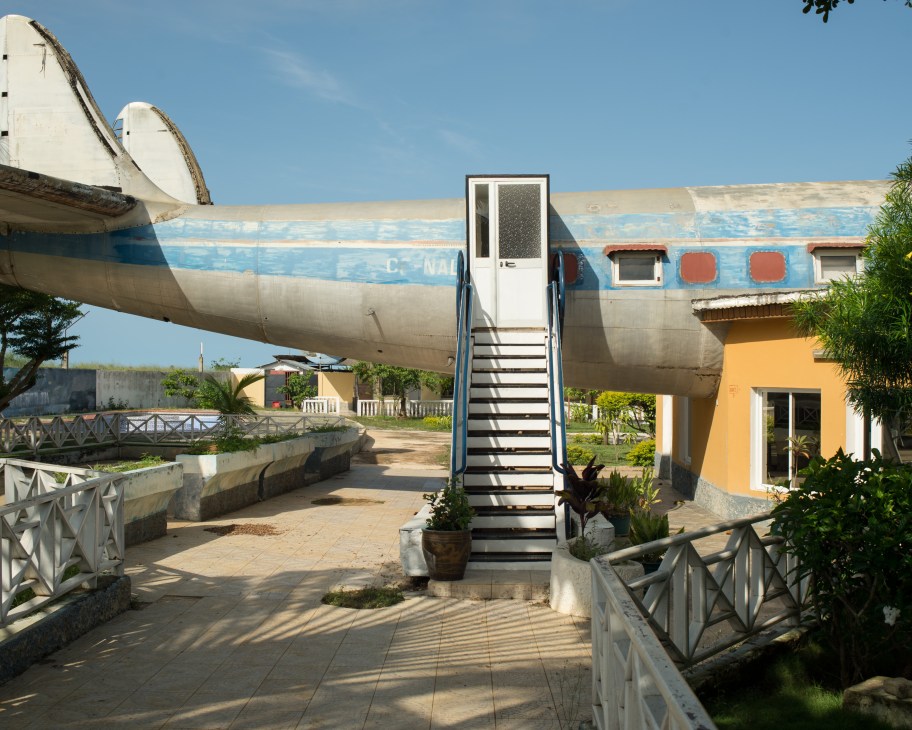 Converted Air Canada plane fuselage repurposed as a bar with entrance stairs and yellow building alongside.