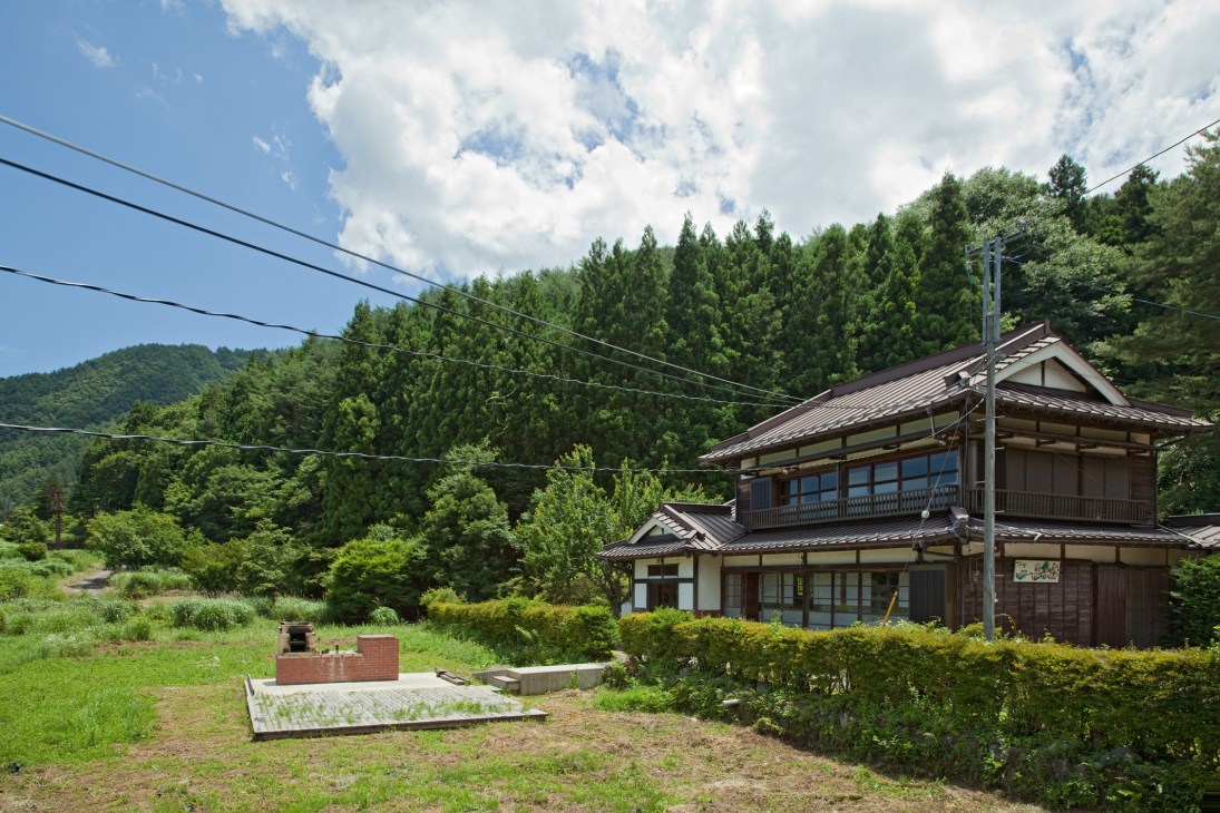 Traditional Japanese wooden house with metal roof nestled in forested landscape near Lake Kawaguchi.
