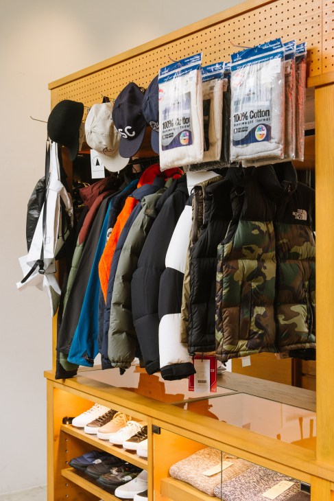 Travel accessory retail display with packaged items, jackets, hats and shoes on yellow wooden shelving.