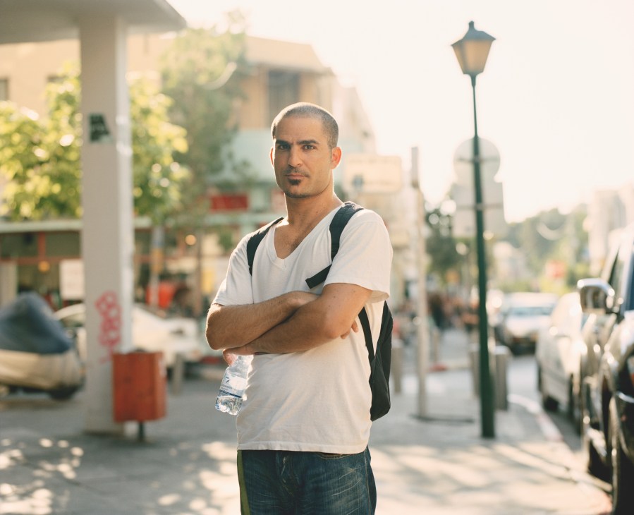 Man in white shirt and backpack standing on a street in Tel Aviv
