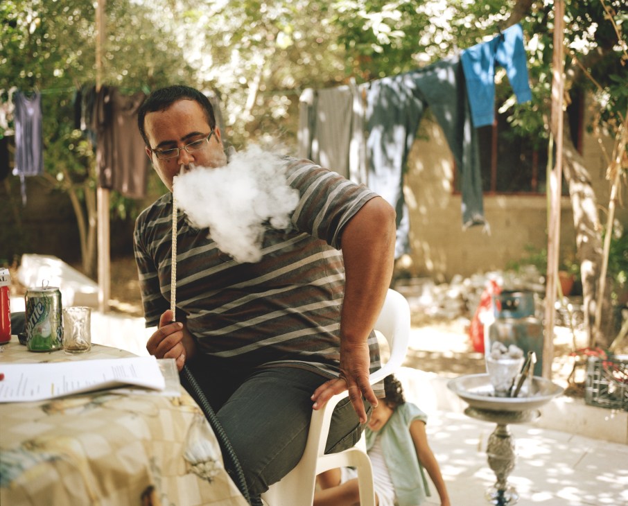 Man in striped shirt smoking shisha pipe with clothesline and courtyard in background