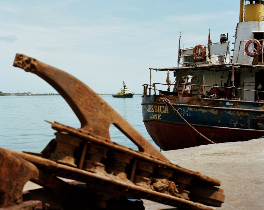 Rusted anchor in foreground with MV Jessica cargo ship docked at São Tomé port.