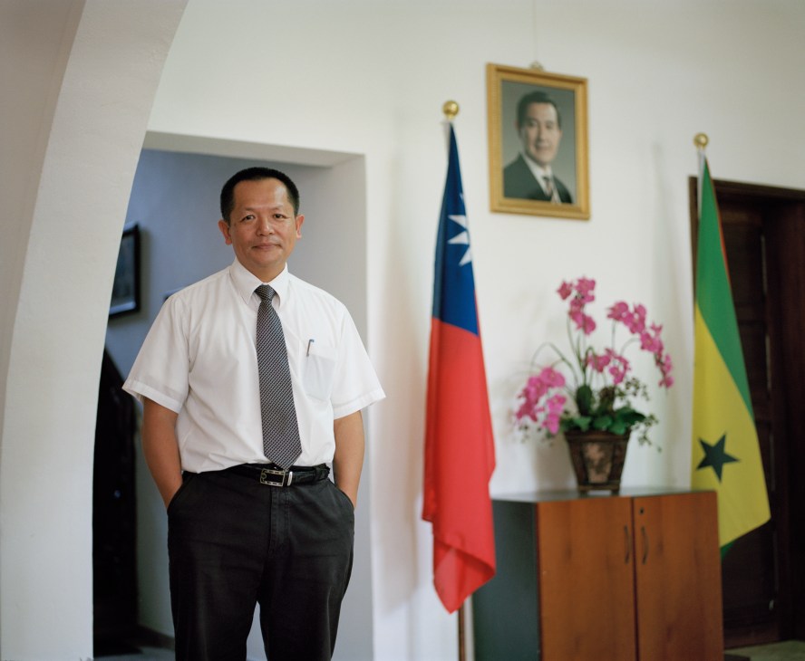Tsung Che Chang, number two at the Taiwanese embassy, stands in formal attire in an official office with Taiwan and São Tomé flags.