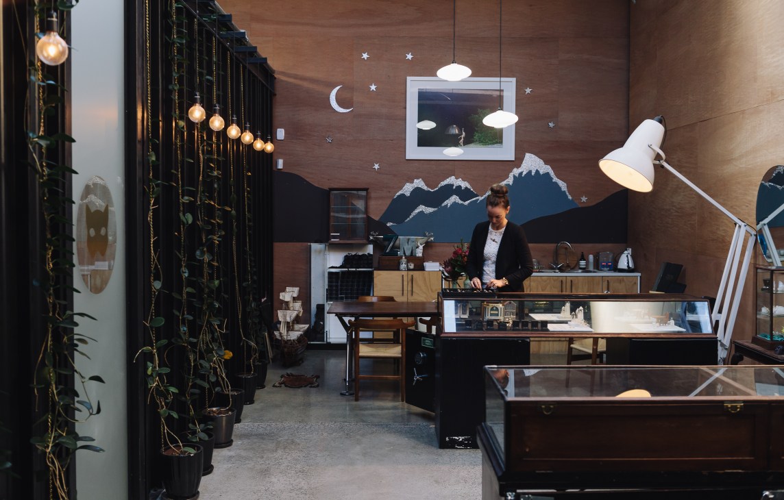 Zoe & Morgan jewellery studio with Victorian display cabinets, hanging plants, and creative wall art featuring mountains and celestial motifs.